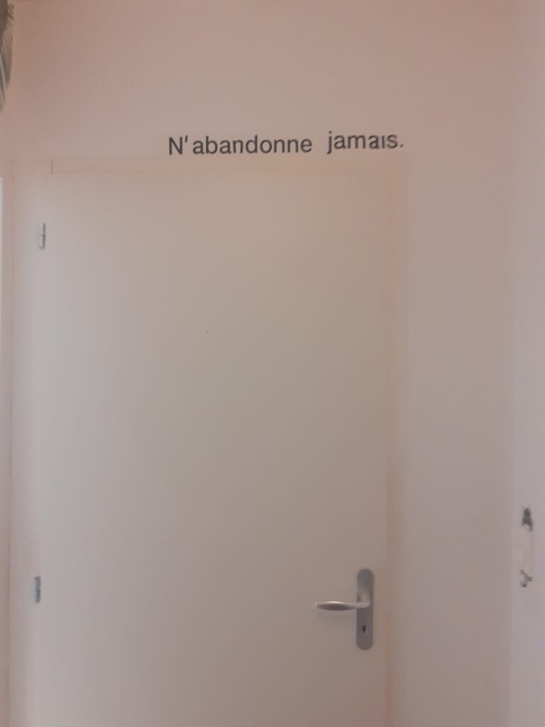 Sticker N’abandonne jamais au-dessus d’une porte de chambre, symbole de résilience et de persévérance